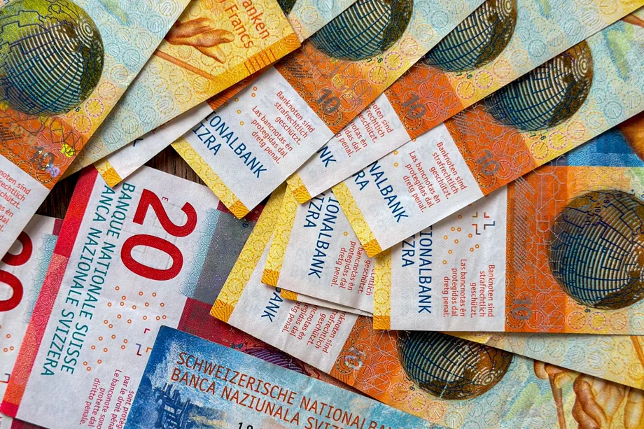 Banconote svizzere da 10, 20 e 100 franchi sparse su un tavolo di legno.