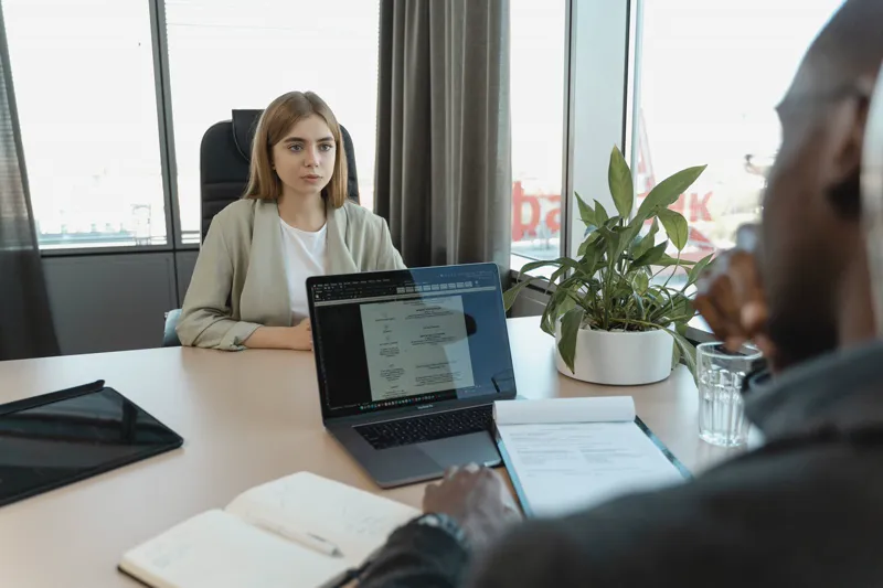 Un recruiter di fronte a una candidata durante un colloquio di lavoro, computer portatile e quaderno sul tavolo.