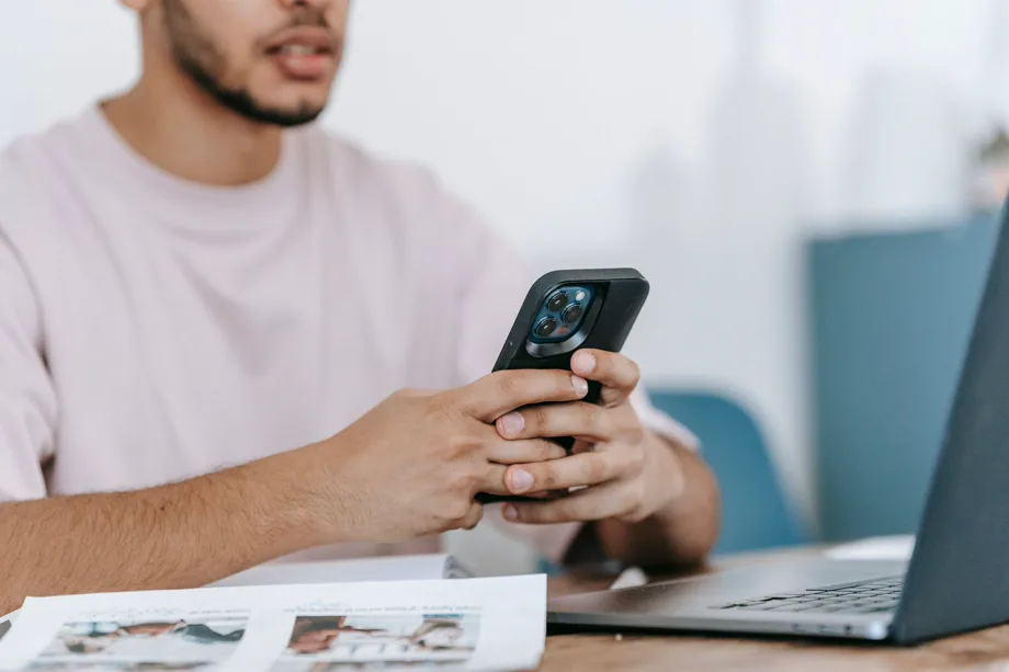 Un candidato consulta un’app di lavoro sul suo smartphone davanti al computer portatile.
