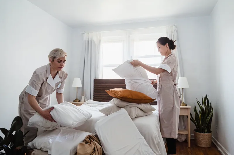 Zwei Zimmermädchen in Uniform machen ein Bett in einem Hotelzimmer, einer der vom Mindestlohn betroffenen Berufe.
